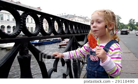 Little girl sucks lollipop at river embankment - Stock Footage [29118490]