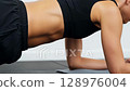 Fit woman in black sportswear performing plank exercise on yoga mat demonstrating core strength training workout routine at home gym 128976004