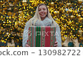 Portrait of cheerful young woman in fur coat holds present box near Christmas tree in town. Pretty blonde lady holds gift enjoying traditional winter fair on Vienna city square 130982722