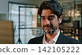 Portrait of Middle Eastern businessman speaks through earbud during client call in modern office. Friendly man listens carefully as answers question with smile Portrait of Middle Eastern businessman speaks through earbud during client call in modern office. Friendly man listens carefully as answers question with smile 142105222