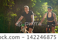 Active couple cycling through sunlit forest trail together, enjoying healthy outdoor exercise Active couple cycling through sunlit forest trail together, enjoying healthy outdoor exercise 142246875